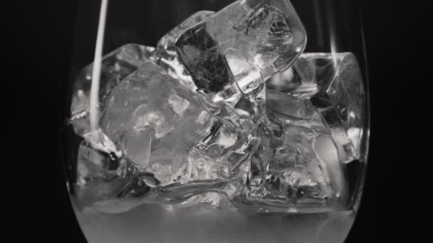 A jégkockák olvasztják az üveg közelségét. Fagyasztott blokkok feltöltése és elárasztása átlátszó csepegtetett borosüveg vízzel. Hideg italok és koktélok makrofekete háttér. Szomjúságcsillapító koncepció - Felvétel, videó