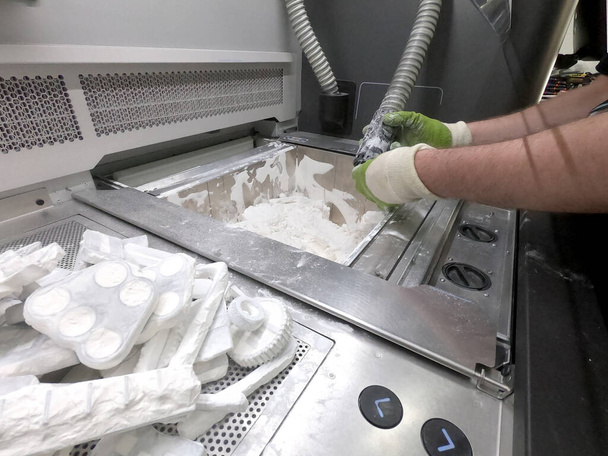 Çalışan bir elektrik süpürgesiyle çalışan bir adam, 3D yazıcının içindeki 3D yazıcıya basılmış bir modeldeki beyaz poliyamit tozunu temizlemek için çalışıyor. Endüstriyel toz 3D yazıcıya basılmış temizleme nesneleri - Fotoğraf, Görsel