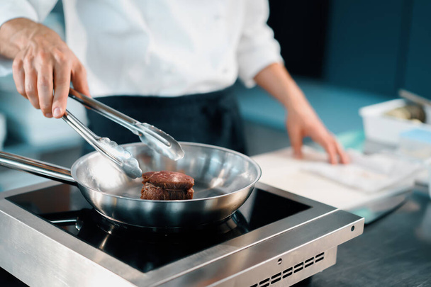 Professional restaurant kitchen, close-up: male chef preparing filet mignon on frying pan - Foto, imagen