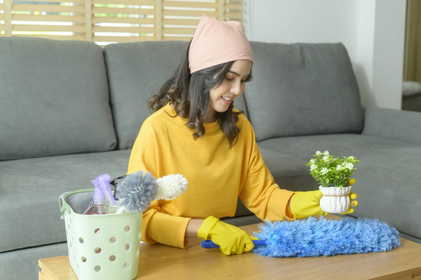 A Young happy woman wearing yellow gloves  and dusting the table in living room. - Foto, Bild