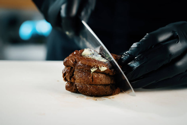 Professional kitchen of a restaurant, close-up: male chef cuts a ready-made delicious filet mignon - 写真・画像