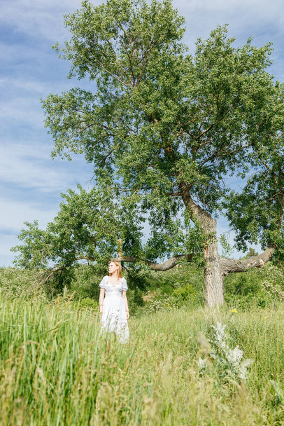 Красивая девушка в белом платье с цветами в поле с видом на небо крупным планом - Фото, изображение