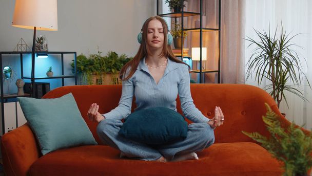 Keep calm down, relax, inner balance. Young woman breathes deeply with mudra gesture, eyes closed meditating with concentrated thoughts, peaceful mind. Tired girl sit at home in living room on couch - Photo, Image