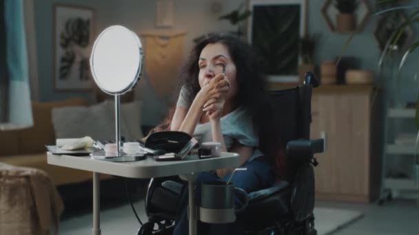 At home woman with spinal muscular atrophy in a wheelchair at the table doing makeup and looking in the mirror - Záběry, video