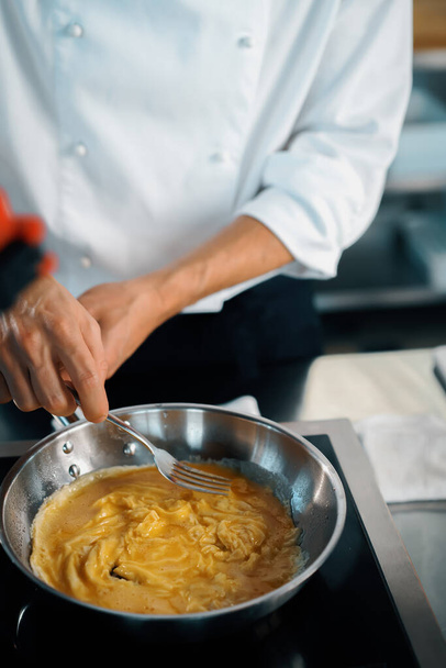 Professional kitchen of a restaurant, close-up: a male chef prepares french omelette in a frying pan - Zdjęcie, obraz