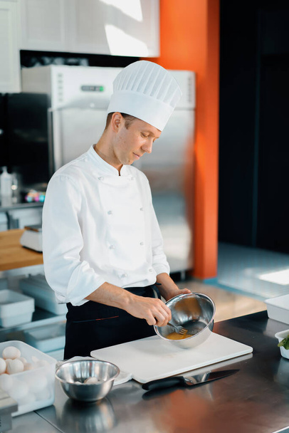 Restaurant professional kitchen: chef prepares delicious dish, beats eggs in a bowl - Fotó, kép