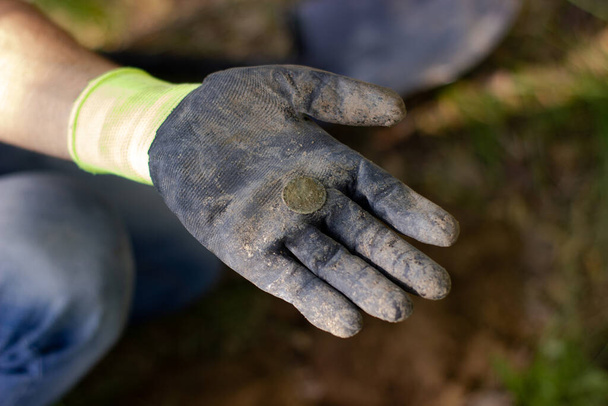 in the palm of a glove lies an old coin found in the ground in a park using a wireless metal detector - Valokuva, kuva