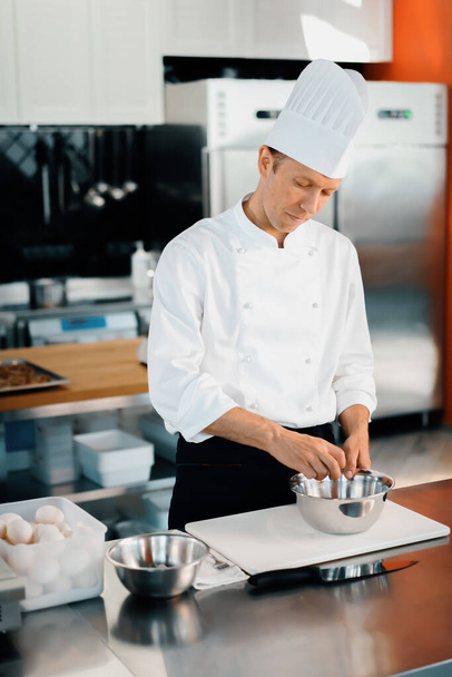 Restaurant professional kitchen: chef prepares delicious dish, beats eggs in a bowl - Foto, Imagen