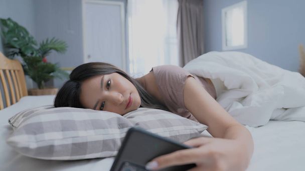 Holiday concept of 4k Resolution. Asian girls don't want to get out of bed in the morning. Mobile phone alarm. Laziness in waking up. - Фото, зображення