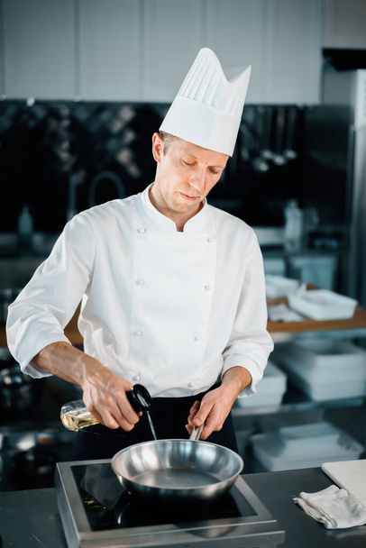 Professional kitchen, male chef splashes oil on hob, frying pan - Fotografie, Obrázek
