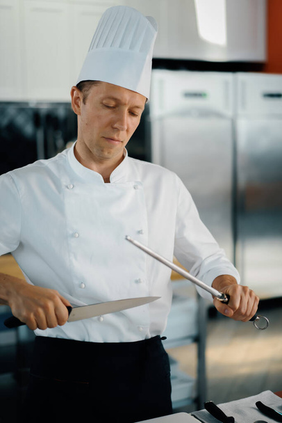 Professional restaurant kitchen, male chef sharpening knife - Valokuva, kuva