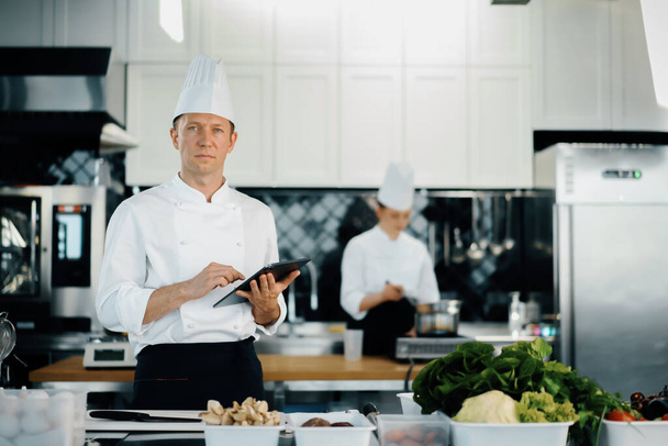 Професійна кухня ресторану, чоловічий шеф-кухар перевіряє наявність продуктів у працівника. Аналітика ресторанного складу. Перевірка попереднього списку
 - Фото, зображення