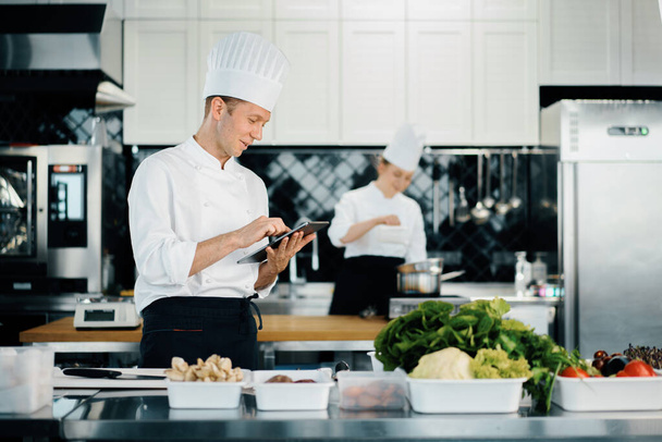 Professional kitchen of a restaurant, male chef checks the availability of products from an employee. Restaurant warehouse analytics. Preaplist checking - Foto, Bild