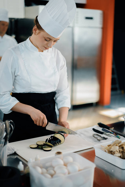 Professional restaurant kitchen, woman chef cuts a zucchini - Photo, image