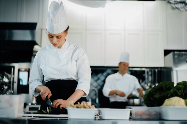 Профессиональная кухня ресторана, женщина-повар режет цуккини - Фото, изображение