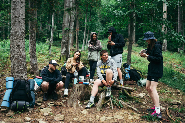 Group of young tourists are sitting in the mountains between the forest and resting during the hike. Friends and active recreation in the mountains. - 写真・画像