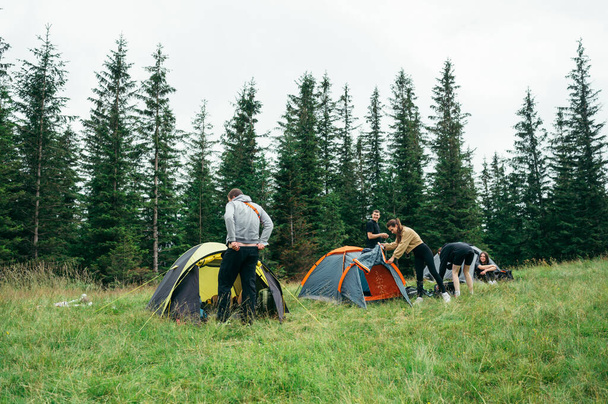 Photo of a camping site of young tourists. A group of tourists pitched tents in the mountains against the background of the forest. - Foto, afbeelding