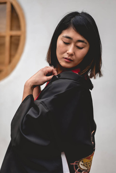 Portrait of sexy and young japanese girl with beautiful old traditional red kimono and black yukata in front of a old white wall in a japanese garden - Fotografie, Obrázek