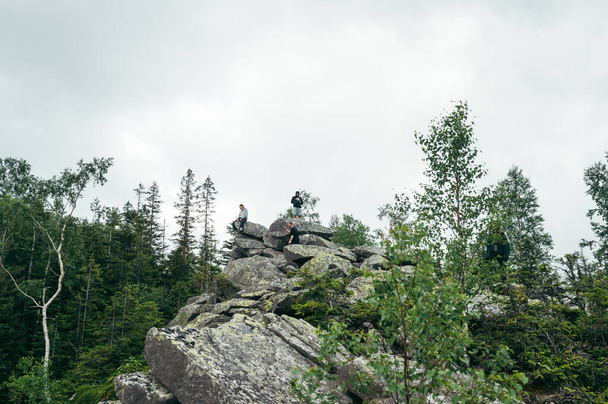 Group of tourists are sitting in the mountains on a rock. Active rest in the mountains, hiking - Фото, изображение