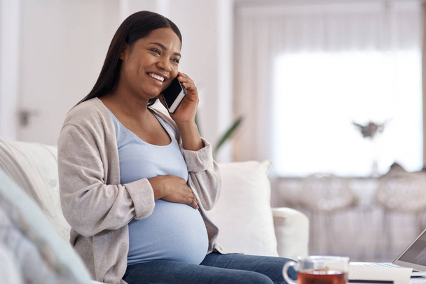 The baby gets excited every time you call. a pregnant woman talking on her cellphone while sitting on the sofa at home - 写真・画像