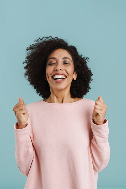 Young black woman laughing while posing with clenched fists isolated over blue background - Photo, image