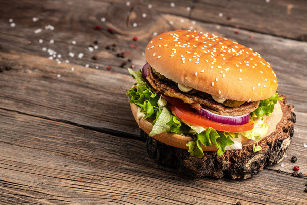 Homemade burger with grilled meat, vegetables, sauce on rustic wooden background. fast food and junk food concept. - 写真・画像