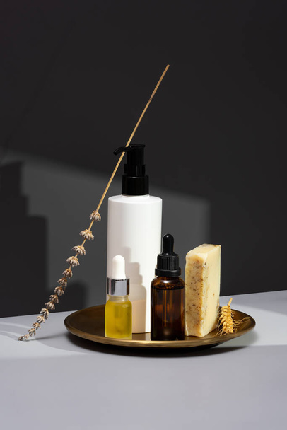 Creative still life with natural cosmetics. Set of essential oils, handmade soap and dried lavender on a dark gray background. The concept of selfcare and organic products. Minimalism, simplistic. - Photo, Image