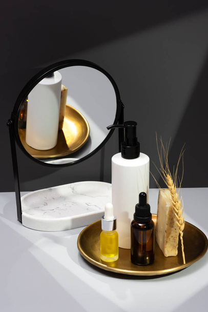 Creative still life with natural cosmetics. Set of essential oils, handmade soap and mirror on a dark gray background. The concept of selfcare and organic products. Reflection in the mirror. - Photo, Image