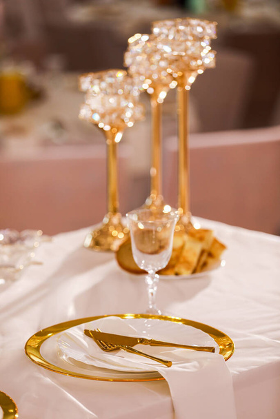 decoración de mesa con mantel rosa, candelabros de cristal con velas y flores de color rosa blanco en el restaurante. elegante día de la boda. mesa de ajuste con placa de oro, tenedor y cuchillo. - Foto, imagen