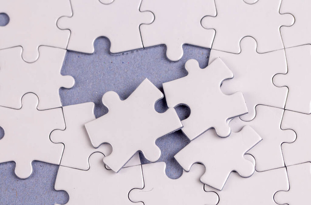 Missing jigsaw puzzle pieces. Business concept. Fragment of a folded white jigsaw puzzle and a pile of uncombed puzzle elements against - Foto, Imagen