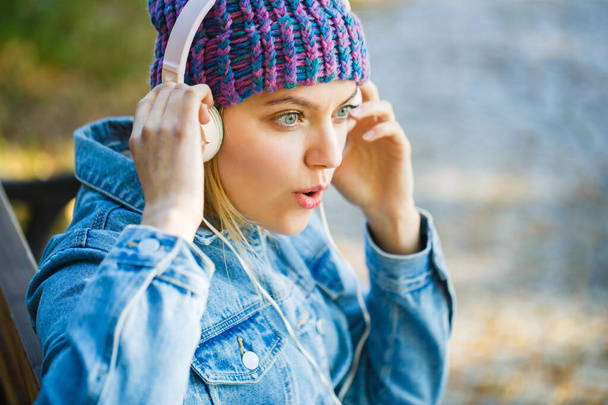 Smiling girl relaxing, music a smartphone and headphones. Outdoors portrait of a trendy girl. Autumn melody concept. Fall cozy atmosphere. Woman with big headphone - Foto, Imagen