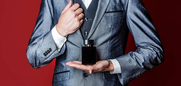 Man holding up bottle of perfume. Men perfume in the hand on suit background. Fragrance smell. - Fotoğraf, Görsel