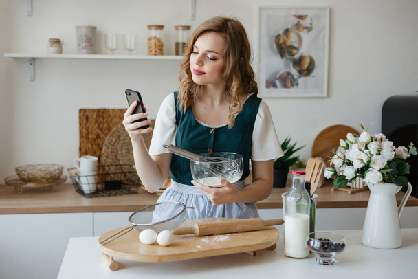 Beautiful girl holding a smartphone in her hand while cooking. High quality photo - Foto, Imagen