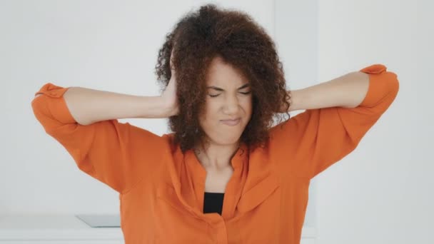Unhappy stressed African American woman with curly hair covers ears with hands holding head feeling annoyed of noisy loud suffer headache pain confused millennial biracial lady refusing hearing sound - Footage, Video
