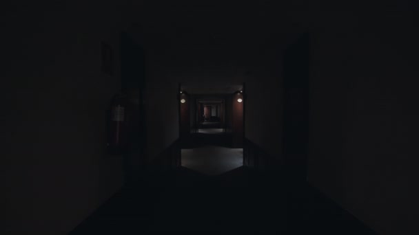 Punto de vista plano de caminar a lo largo del pasillo oscuro y luego las luces encendidas. Pasillo vacío del hotel con paredes blancas y puertas de madera oscura. Alojamiento confortable - Metraje, vídeo