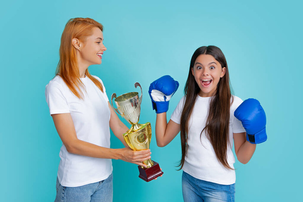 Mommy and teenager child daughter holding winning prize, showing trophy against blue background. Parent support girl child, celebrating victory. Teenager boxer winner boxing - Foto, immagini