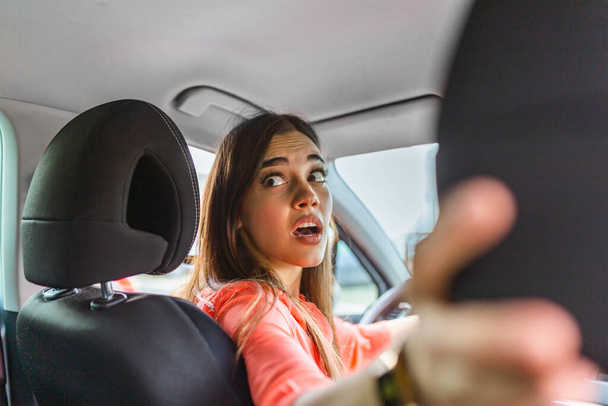 Woman in car turning around looking at passengers in back seat idea taxi driver. Concept of exam Vehicle. Back view of an attractive young businesswoman looking over her shoulder while driving a car. - Foto, imagen