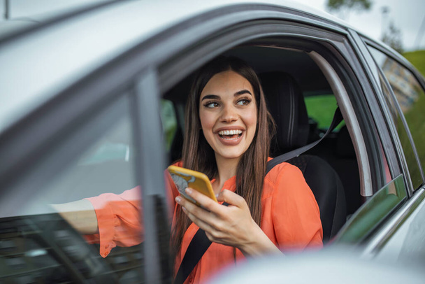 Young girl uses a mobile phone in the car. Technology cell phone isolation. Internet and social media. Woman with smartphone in her car. Girl is using a smartphone - Фото, изображение