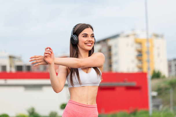Athletic young woman with towel smiling and streaching. Young sporty woman training. Woman Doing Workout Exercises On Street . Fit girl streaching before active fitness training - Foto, immagini