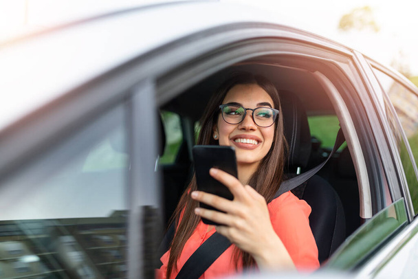 Woman driver using a smart phone in car. Woman driver using a smart phone in car. Leisure, road trip, technology, travel and people concept - Happy woman driving car with smartphone - Fotografie, Obrázek