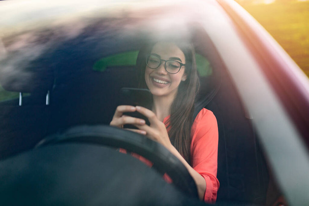 テキストと運転、ホイールの後ろ。法律を破る。車を運転している女性は携帯電話に気を取られている。車の中で待っている間に電話でメッセージを入力する女性. - 写真・画像