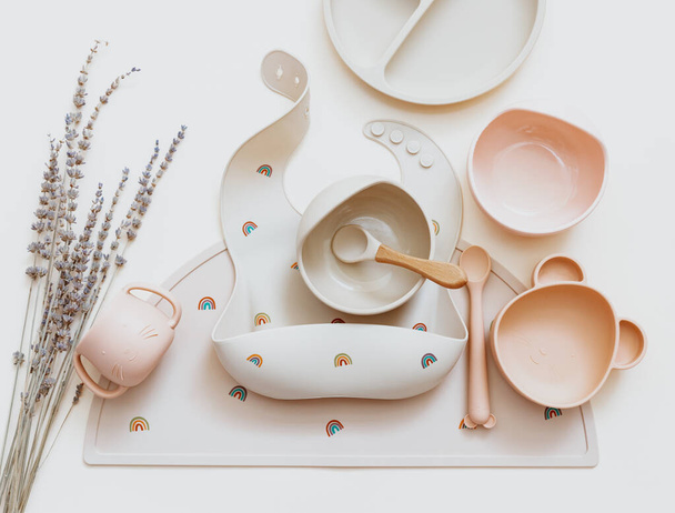 Flat lay composition with silicone set tableware for baby, bibs and plate on beige background. Serving food. Concept of kids menu, nutrition and feeding - Foto, Bild