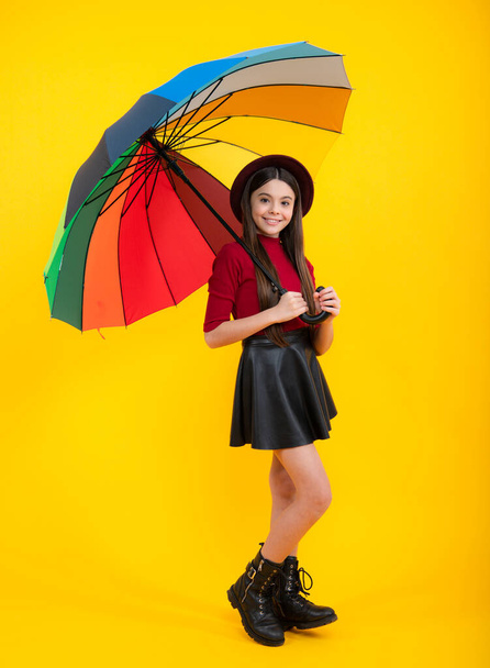 Fashion autumn weather for children. Teenager girl with umbrella in autumn skirt, sweater, boots and hat isolated on yellow studio background. Autumn trendy teen kids clothes - Φωτογραφία, εικόνα
