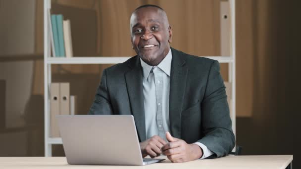 Old African 60s happy businessman laughing smiling sitting at office with laptop make you are right sign agree support good idea gesture approve nod head yes talking at camera video call conference - Felvétel, videó