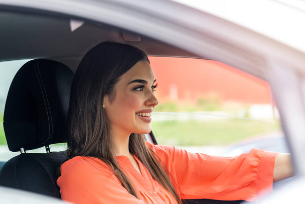 Cute young lady happy driving car. Image of beautiful young woman driving a car and smiling. Portrait of happy female driver steering car with safety belt"n - Foto, Bild