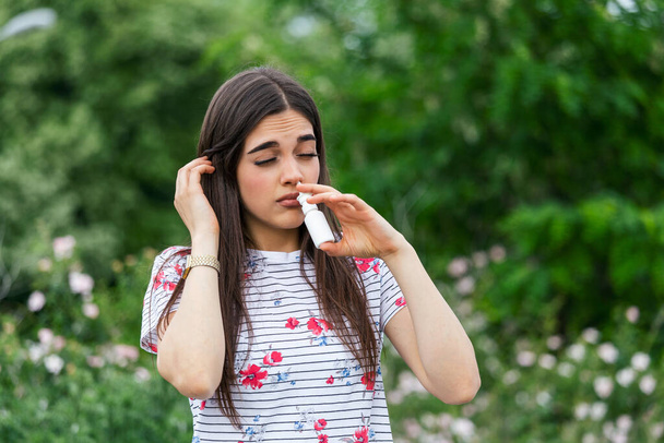 Pollen allergy concept. Young woman using nose spray for her pollen and grass allergies. Flowering trees in background. Spring Seasonal allergies and health problems. - Foto, immagini