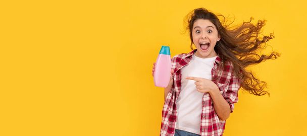 happy teen girl with long curly hair hold shampoo bottle, hairdresser. Banner of child girl hair care, studio poster header with copy space - Foto, afbeelding