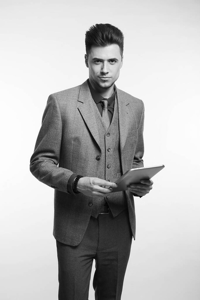 Atractivo hombre de negocios sonriendo y sosteniendo su tableta mientras usa una corbata roja y un traje azul, de pie sobre fondo blanco del estudio
 - Foto, Imagen