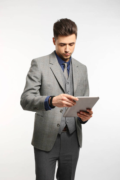 Привлекательный бизнесмен улыбается и держит планшет в красном галстуке и синем костюме, стоя на белом фоне студии
 - Фото, изображение