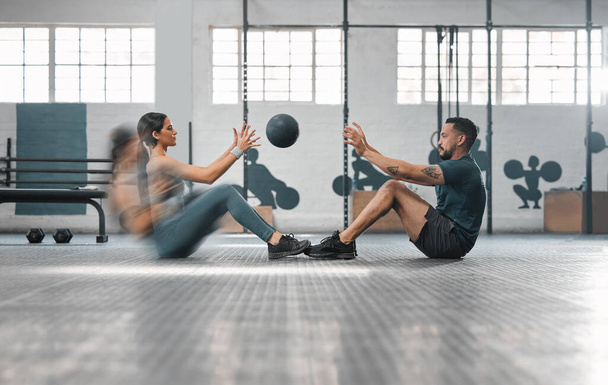 Active, sporty fitness couple or gym partners training together, doing abs exercises by throwing a weighted slam ball. Male trainer and female athlete in motion focused on workout session or class - 写真・画像